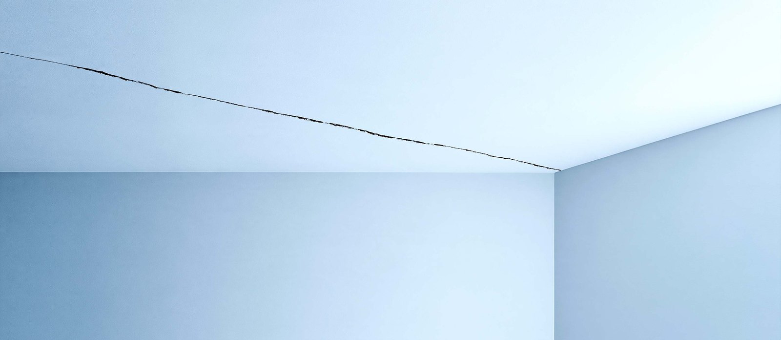 A long crack across a white ceiling above blue walls.