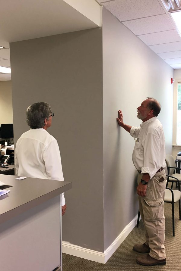 Two adults inspecting a finished drywall partition in an office.