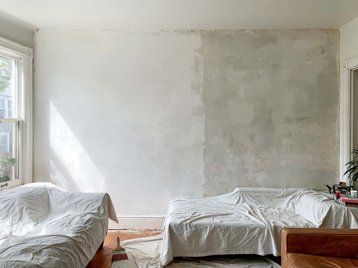 A partly skim-coated wall behind furniture protected with drop cloths.