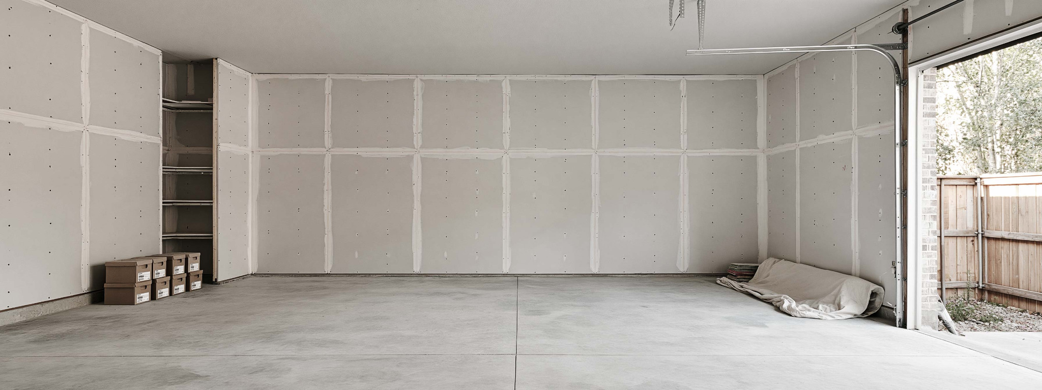 A cleared garage with unfinished drywall, stored boxes and a folded drop cloth.